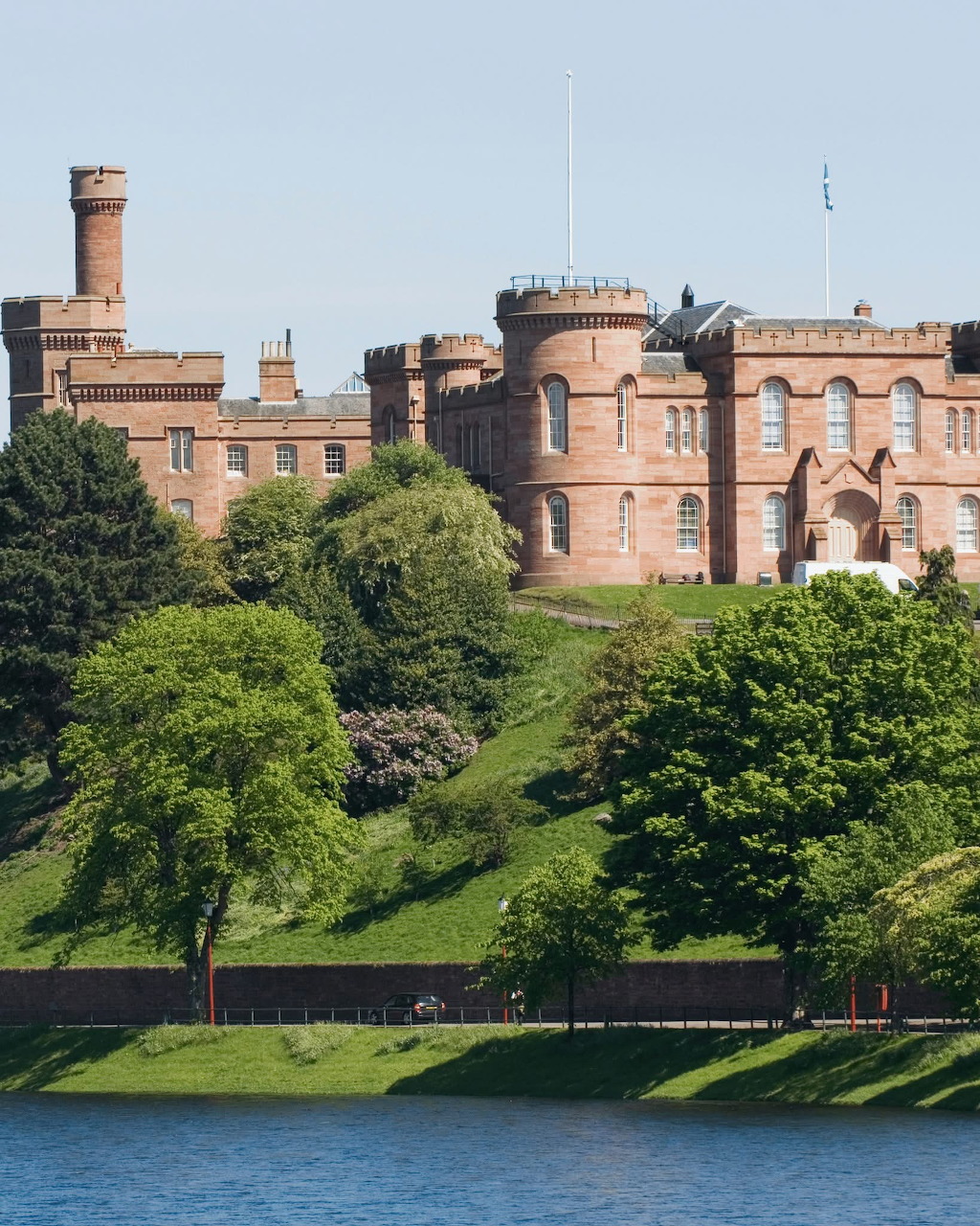 Red sandstone Inverness Castle on a hill above the River Ness, Scotland, with green trees and blue water