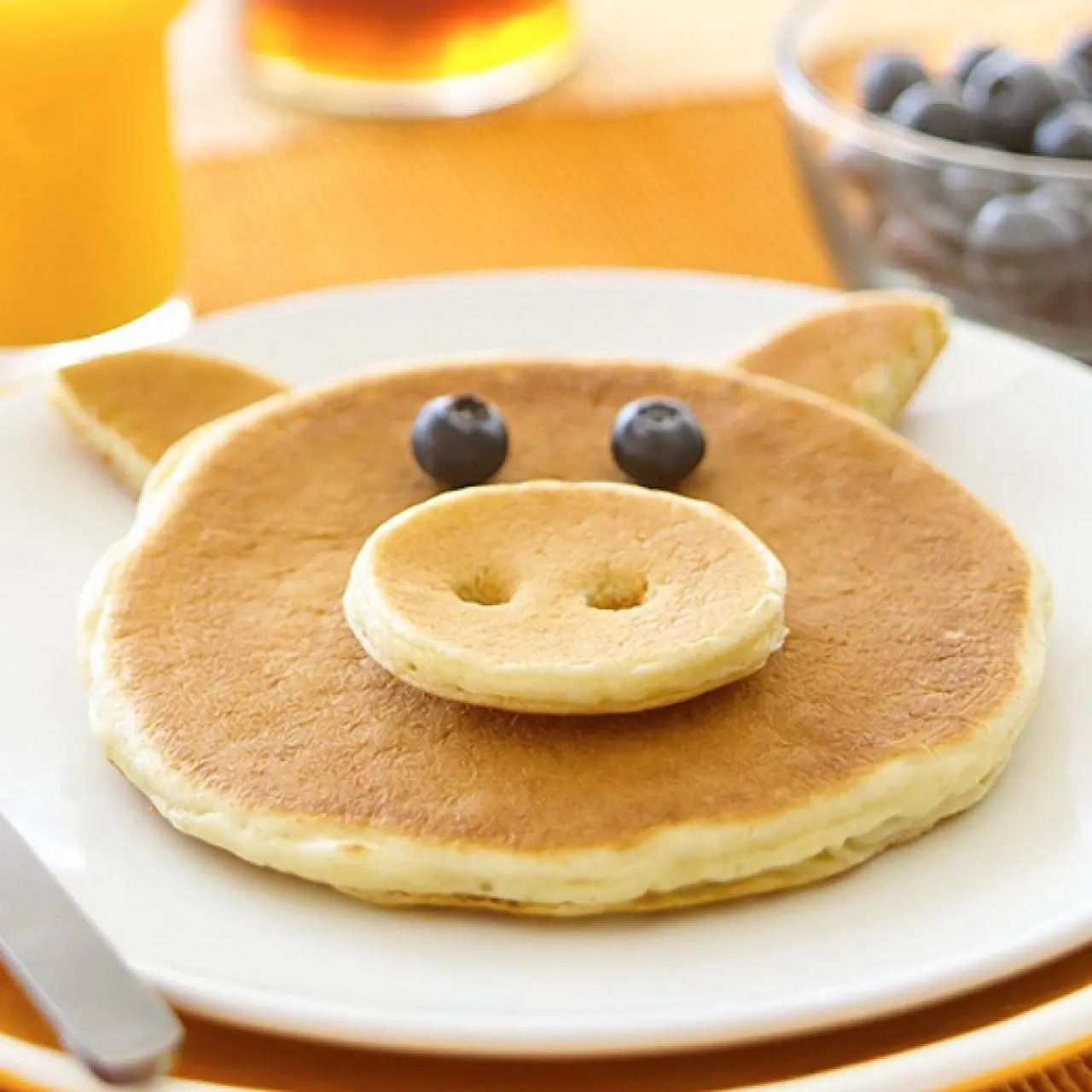 Pig-shaped pancakes on a white plate with blueberries for eyes and a small pancake snout