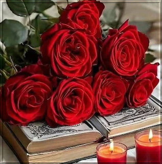Bouquet of red roses lying on an ornate vintage book with glowing candles in front