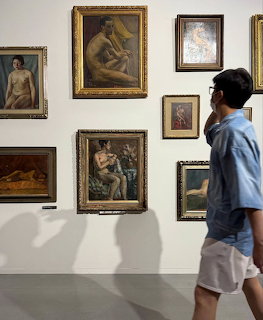 Person in blue shirt viewing framed paintings on white gallery wall