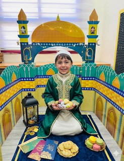 Smiling child in green traditional outfit sitting in front of a colorful cardboard mosque display with golden dome