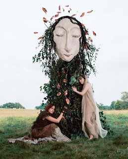 Woman with large sculptural head kneeling in field with dark flowing hair and autumn leaves