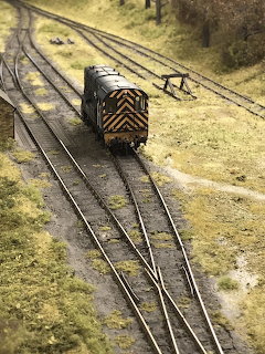 Model train locomotive on curved tracks in a detailed miniature railway scene