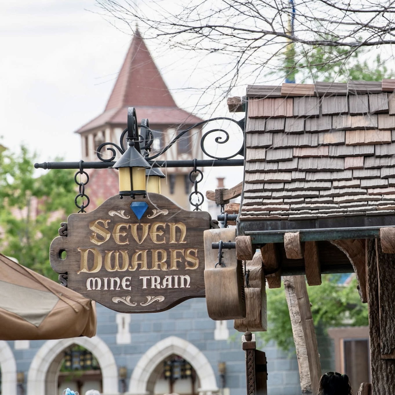 Wooden sign reading 'Seven Dwarfs Mine Train' with ornate lamp fixture and themed building in background