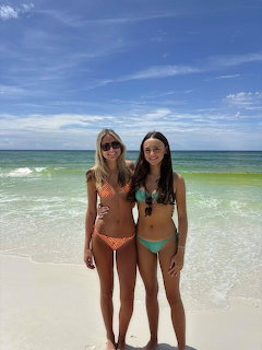 Two women in bikinis standing together on a white sand beach with turquoise ocean behind them