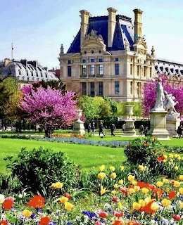 Jardin des Tuileries in Paris with colorful flowers, pink blossoming trees, and the Louvre palace behind