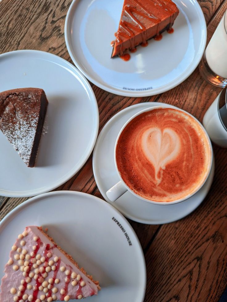 Overhead view of latte art coffee with three slices of cake on white plates on a wooden table