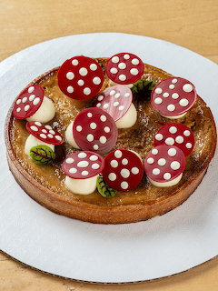 Chocolate tart decorated with red mushroom cookies with white polka dots and green mint leaves
