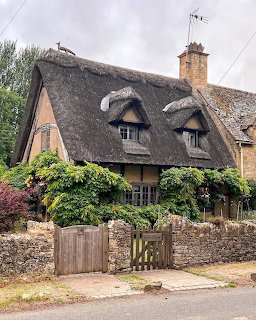 Historic thatched roof cottage with stone walls and garden gate in English village