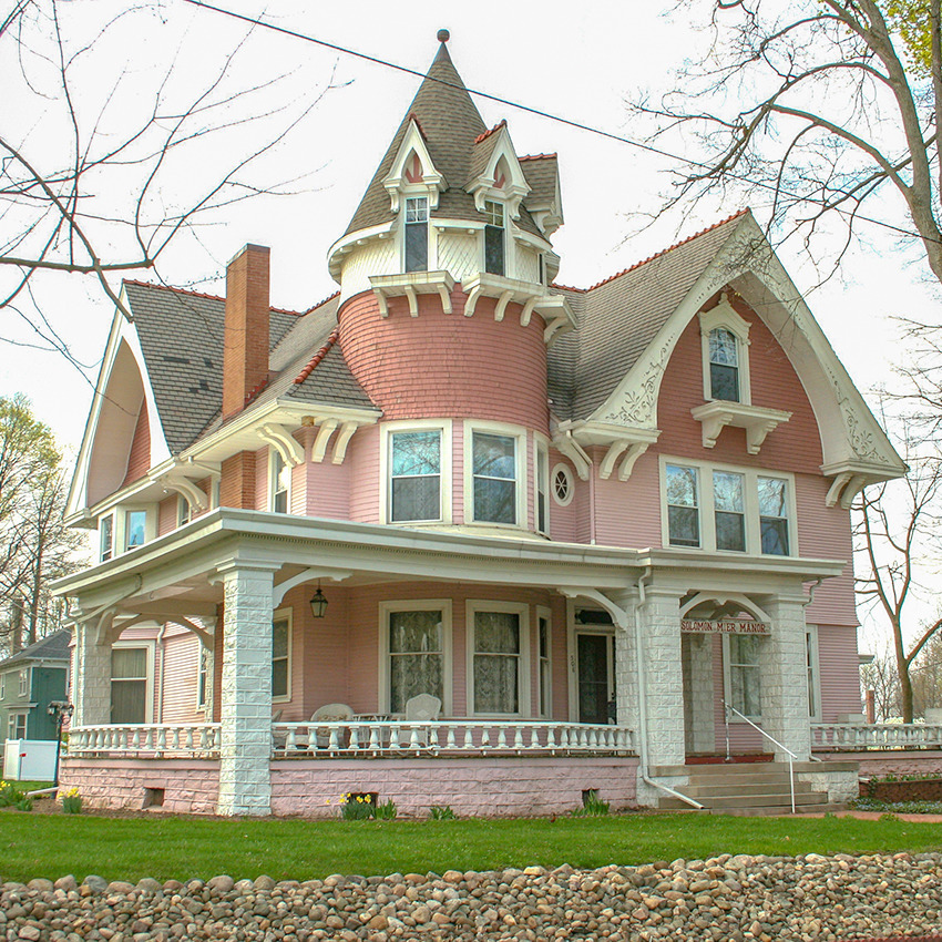 Pink Victorian house with white trim, turret, and wraparound porch on green lawn