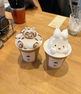 Two coffee cups with adorable 3D foam art shaped like cute animals on a wooden cafe table