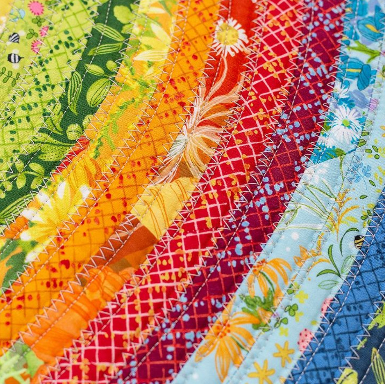 Diagonal strips of rainbow-colored quilting fabrics with various floral and geometric patterns arranged side by side