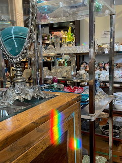 Antique shop interior with glassware, ornate lamp, and rainbow prism light on a wooden counter