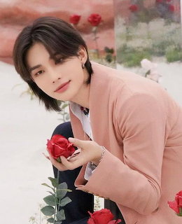Young man in pink blazer holding a red rose with roses scattered around him