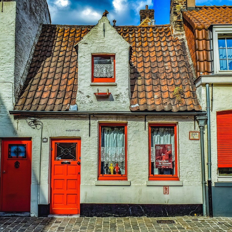Row of quaint Belgian houses with orange tile roofs, white walls, red doors, and cobblestone pavement