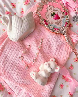 Pink pleated top with a decorative hand mirror, white swan vase, bear figurine, and beaded necklace on floral background