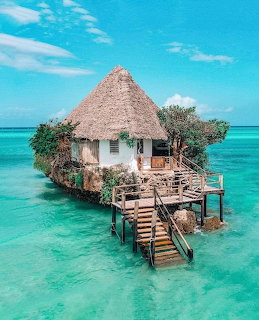 Thatched restaurant building on small rock island surrounded by turquoise ocean water with wooden pier