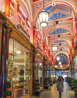 Victorian shopping arcade with arched glass roof, ornate columns, and illuminated shop windows in London