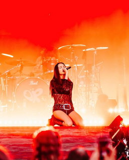 Female singer kneeling on stage with microphone under red and orange concert lights