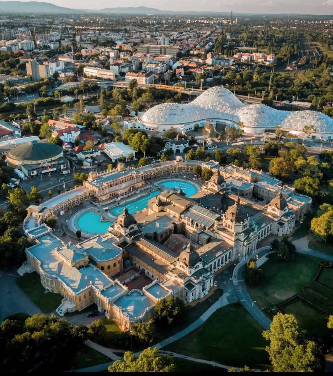 Aerial view of ornate Budapest thermal baths complex with multiple pools surrounded by historic buildings and greenery