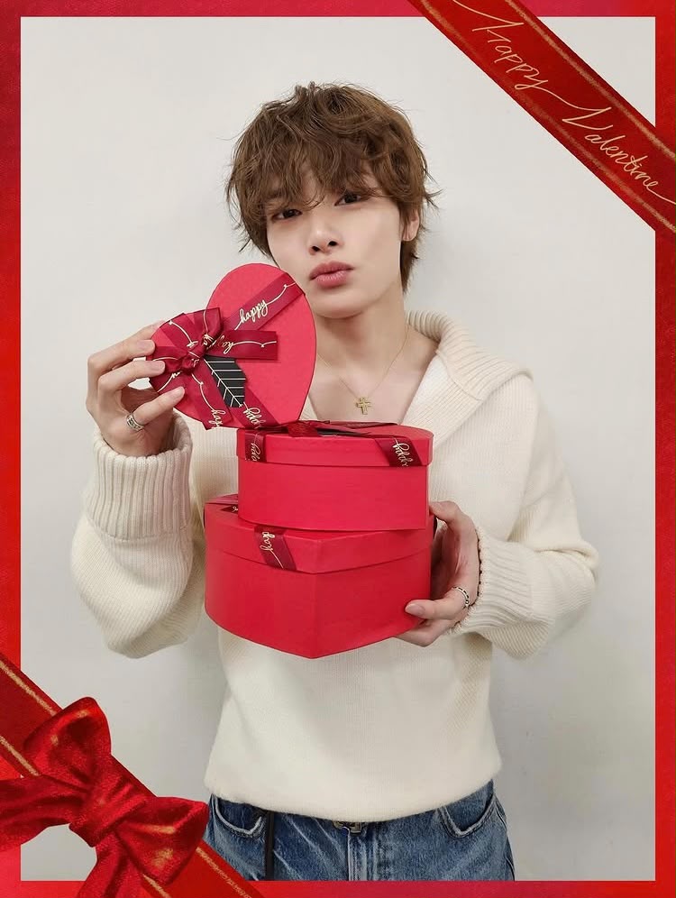 Young person holding a red heart-shaped gift box while wearing a white sweater