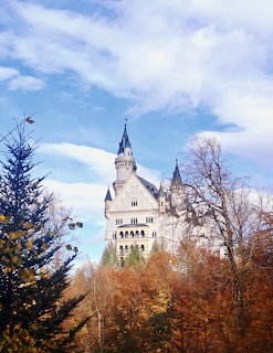 Neuschwanstein Castle rising above colorful autumn trees against a cloudy blue sky