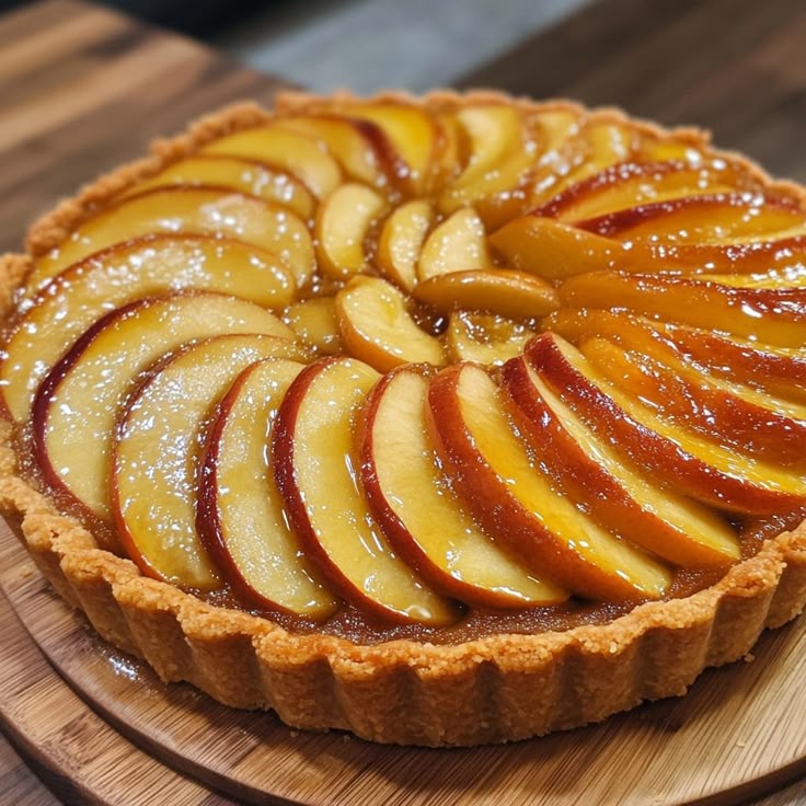Apple tart with spiral-arranged sliced apples on golden crust, glazed and dusted with sugar on wooden board