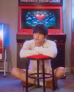 Young man with dark hair sitting on a red stool in front of a retro arcade machine with pixel heart display