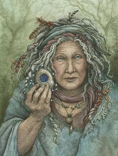 Painted elderly woman with wild gray hair holding a blue eye pendant in front of a soft forest backdrop.