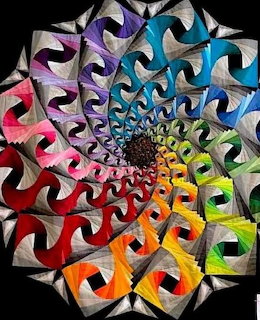 Colorful spiral quilt design with rainbow ribbon shapes radiating outward on black background