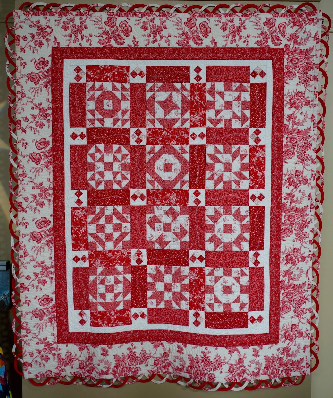 Red and white patchwork quilt with geometric patterns and pink floral border