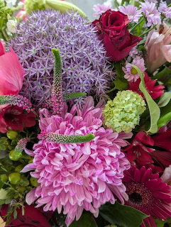 Close-up of a colorful flower bouquet with pink chrysanthemums, purple allium, red roses, and green accents
