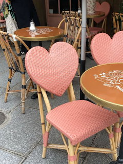 Pink heart-shaped wicker cafe chairs beside round tables on a sidewalk terrace