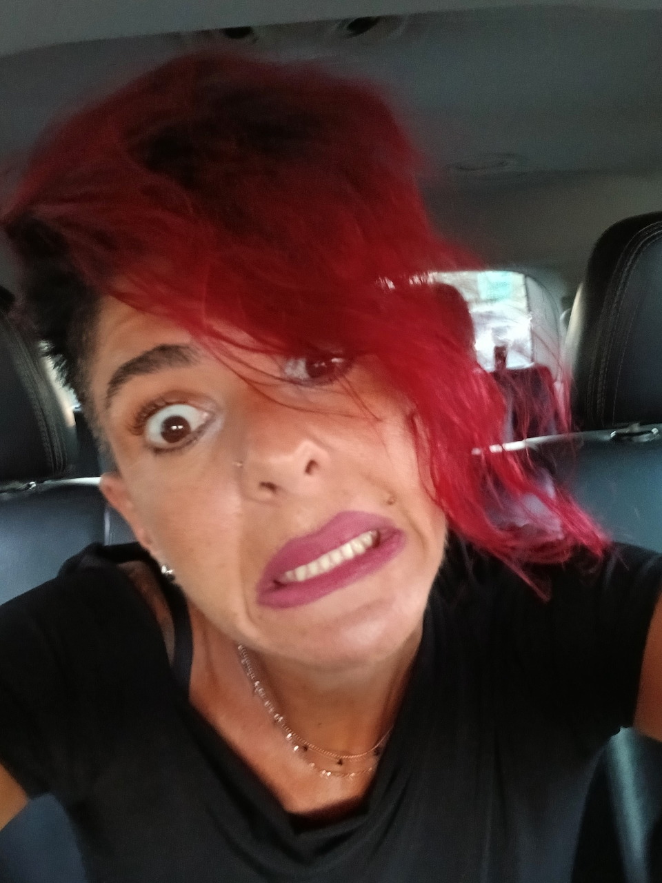 Woman with bright red hair making a funny wide-eyed face in a car selfie