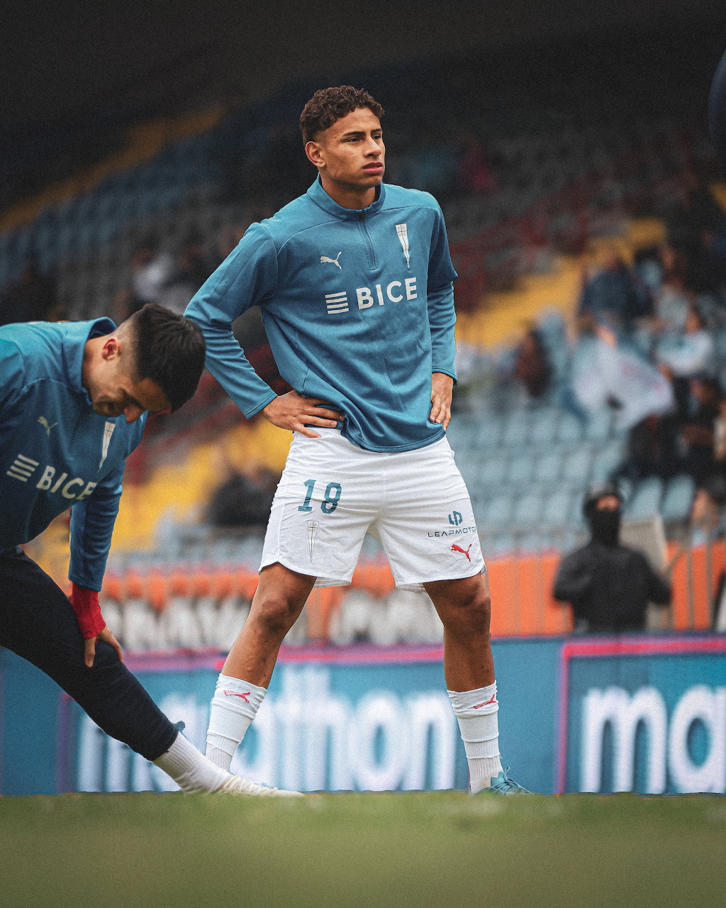 Soccer player in teal BICE jersey number 19 stretching during warm-up at a stadium