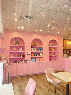 Pastel pink cafe interior with arched shelves, hanging flowers, tables, and chairs
