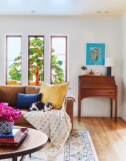 Living room with three colorful stained glass windows, yellow armchair, wooden dresser, and hardwood floor