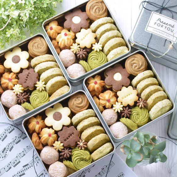 Overhead view of four square boxes filled with assorted decorated cookies including swirls, flowers, and sandwich cookies
