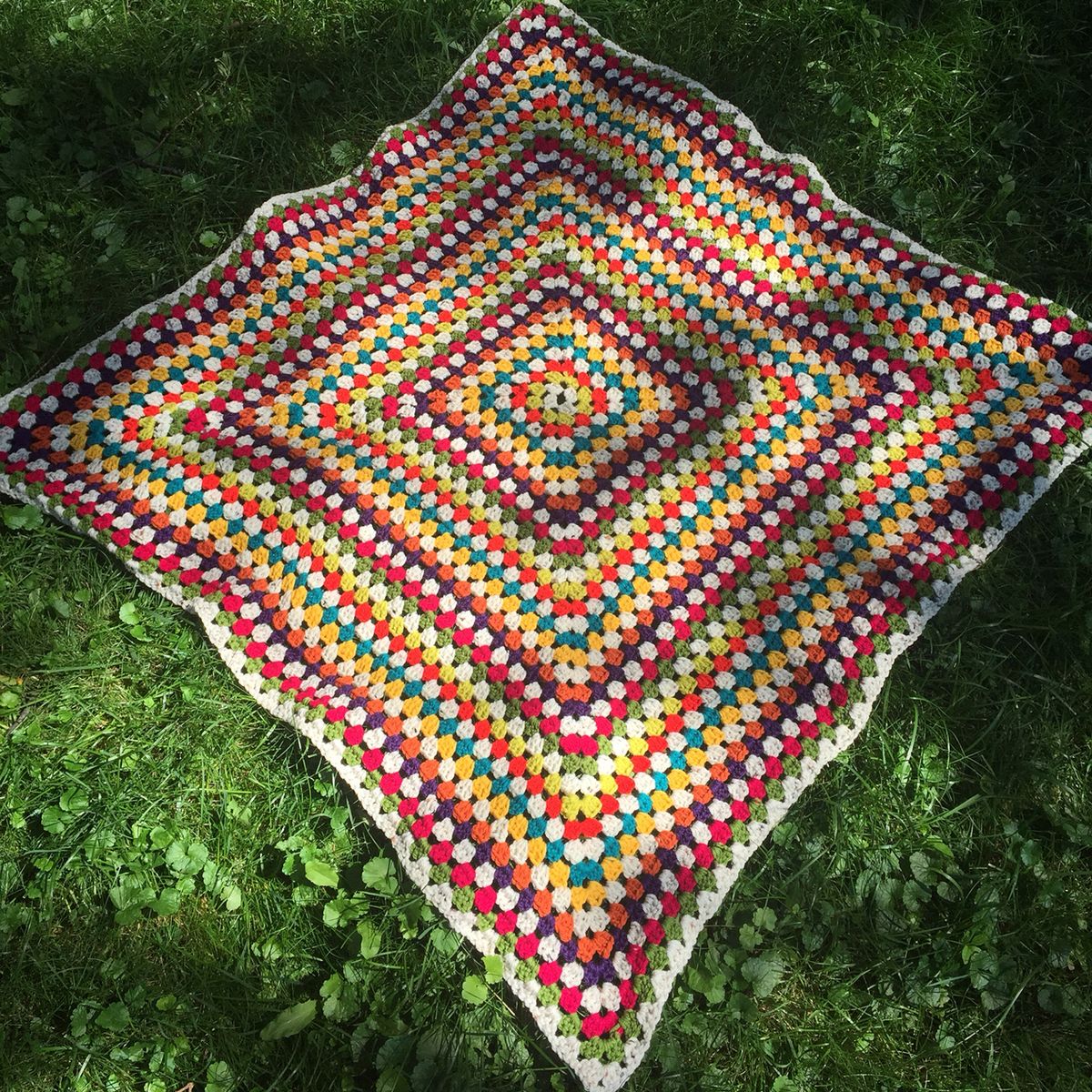 Colorful crocheted granny square blanket with rainbow stripes on grass