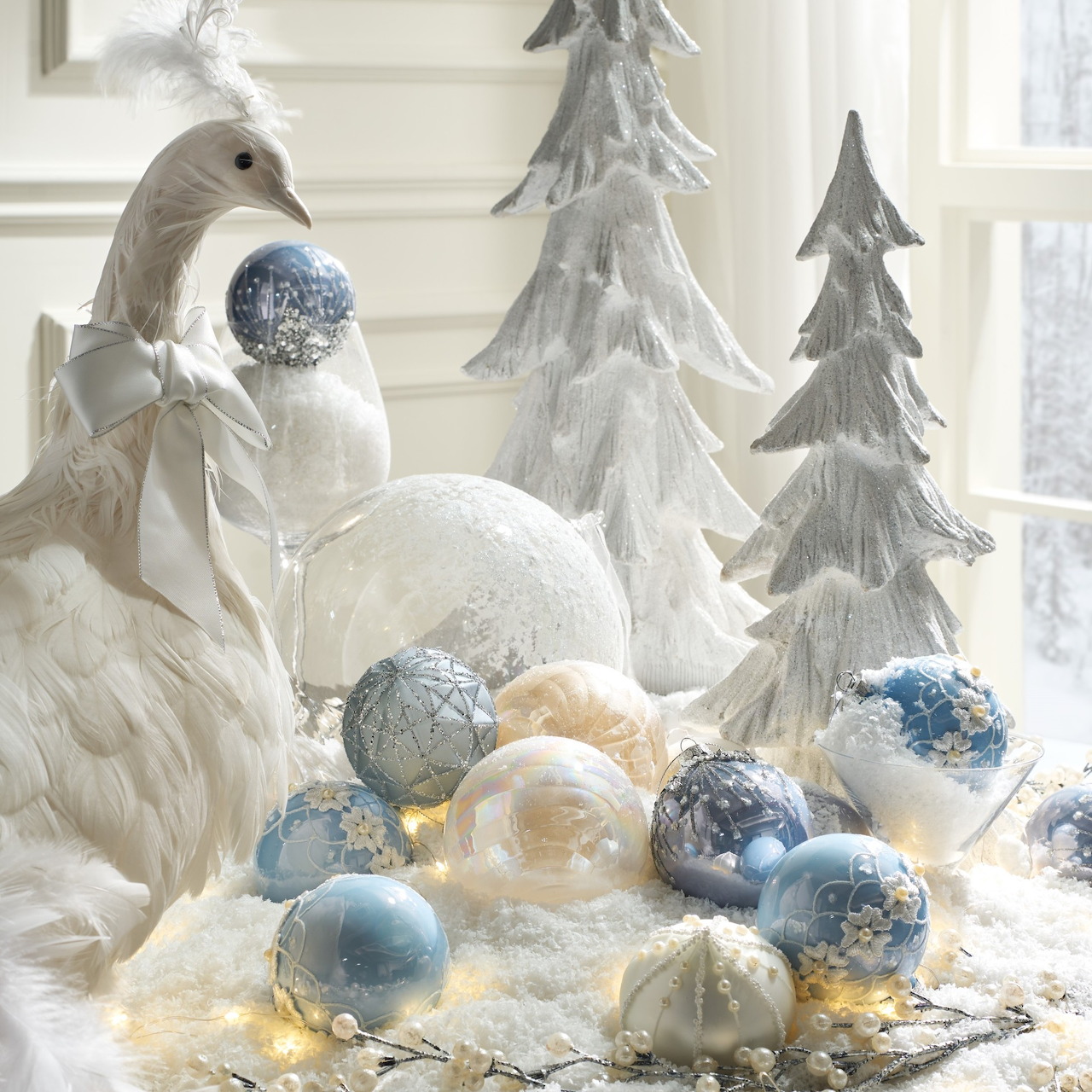 White Christmas display with frosted trees, ornaments, faux snow, and a white bird by a window