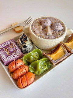 White tray with Korean desserts including purple rice cake, green tteok, poridge bowl, and colorful sweets