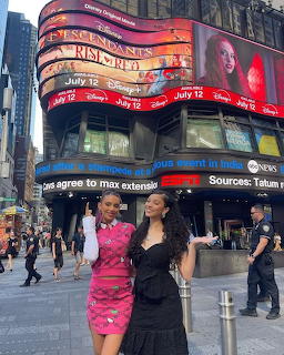 Two women posing in Times Square with large billboards and a busy street behind them
