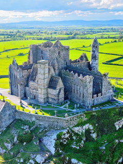 Stone castle ruins on a grassy hill with bright green fields and blue sky