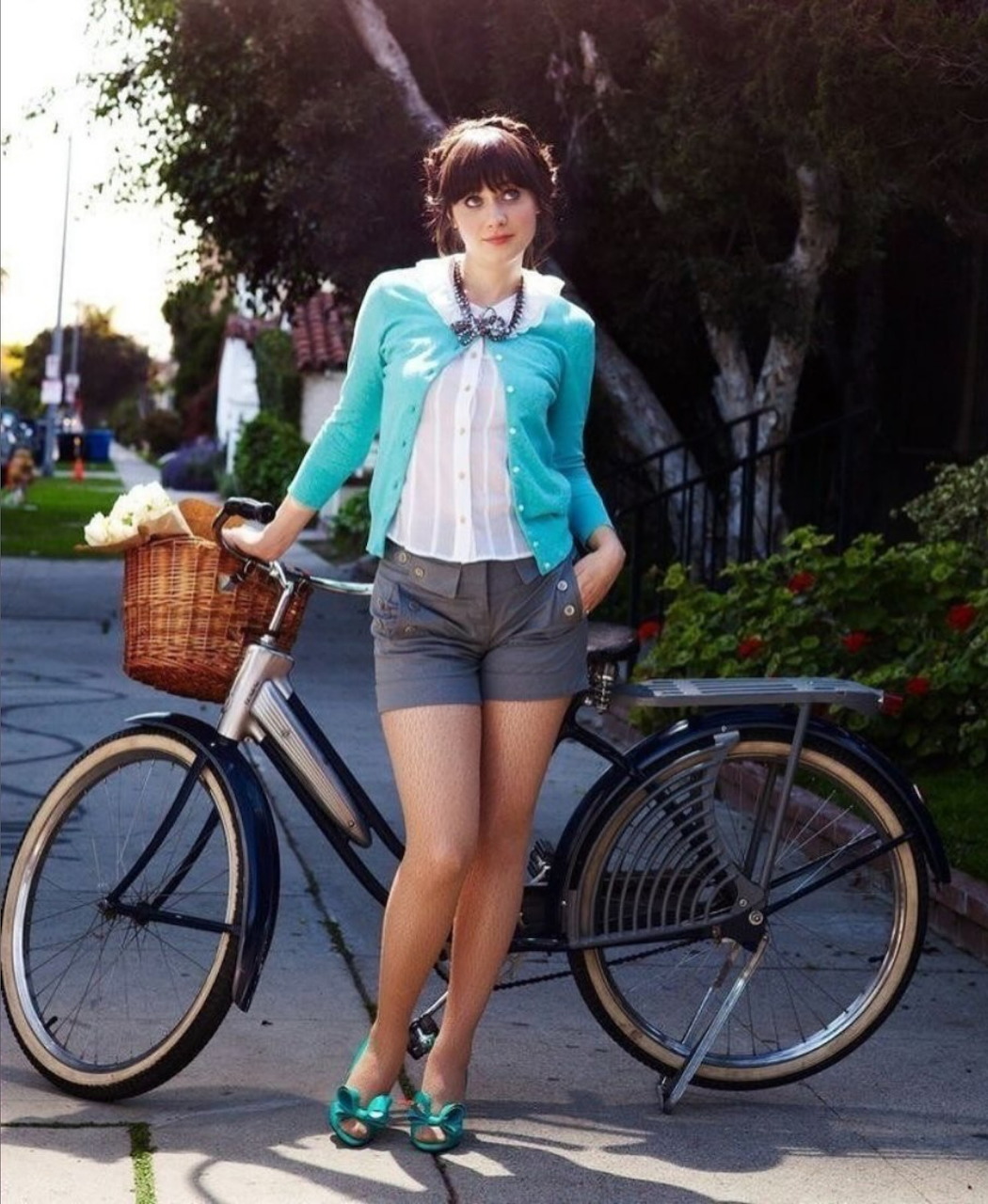Zooey Deschanel standing beside a vintage bicycle on a sidewalk in casual summer clothes