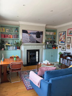Cozy living room with blue sofa, fireplace, teal built-in bookshelves, dining table, and framed artwork