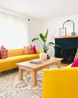 Modern living room with two yellow sofas, wooden coffee table, black fireplace, and banana leaf plant
