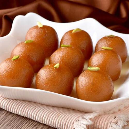 Six round gulab jamun dessert balls with pistachio garnish on white plate