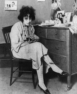 Black and white vintage photo of a woman in 1920s attire seated by a wooden dresser