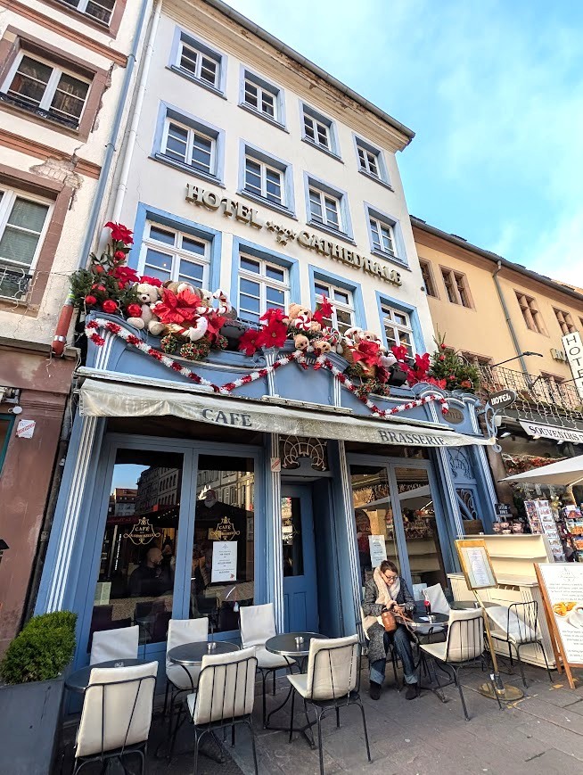Blue-fronted café with outdoor terrace beneath a flower-decorated hotel building on a European street