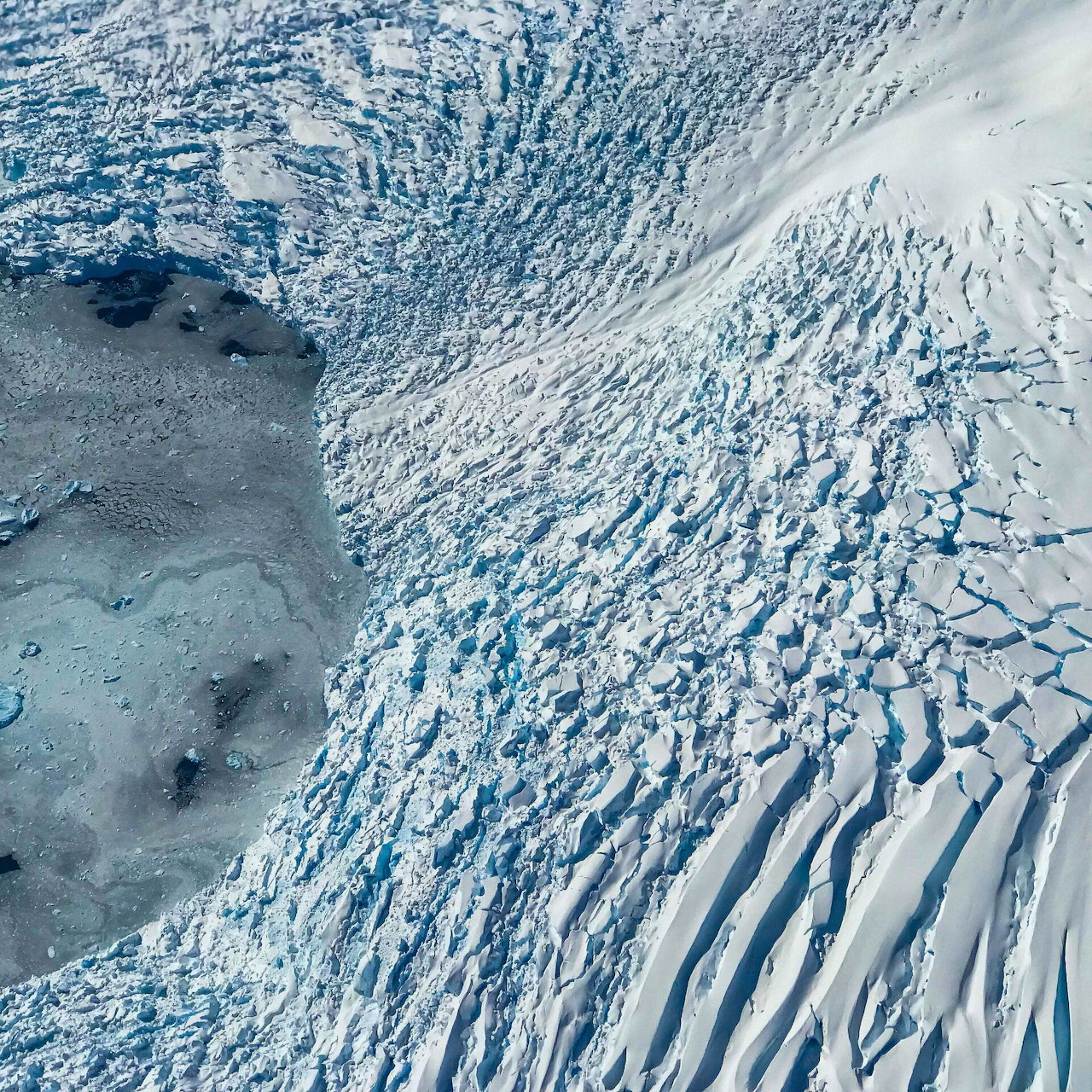 Aerial view of a fractured Antarctic ice sheet with ridged snow and a gray icy edge